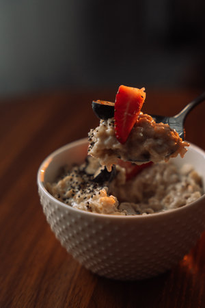Oatmeal with strawberries in a white bowl on wooden background.