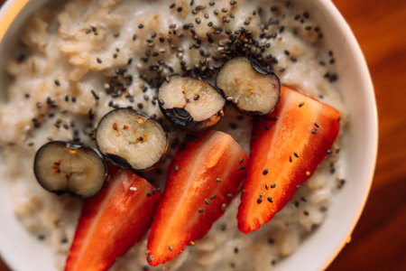 Oatmeal with strawberries in a white bowl on wooden background, close up