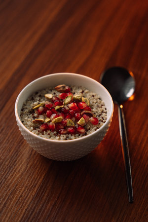 quinoa porridge in a white bowl with pomegranate and nuts, vertical photo.