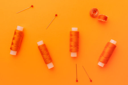 Orange sewing threads and pins on bright background