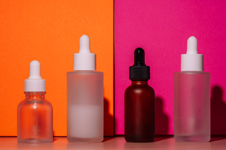Assorted glass dropper bottles on orange and pink background. Beauty product mockup.