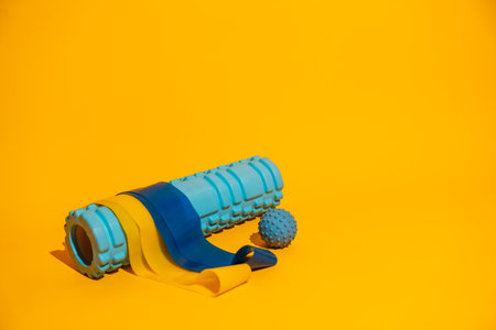 Foam roller with resistance bands and massage ball on vivid yellow background wellness recovery copy...