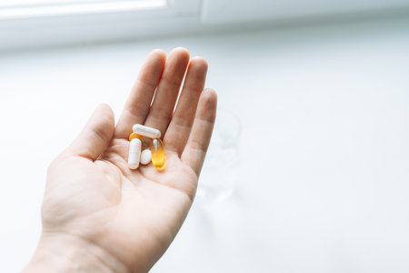 Hand holding assorted vitamins and capsules by a bright window on white backgroundの写真素材