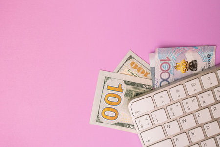 Computer keyboard with US dollars and Kazakhstani tenge on pastel pink backgroundの写真素材