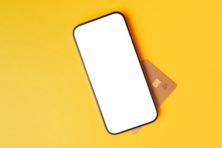 Minimal mobile-payment concept: a modern smartphone with a blank white screen rests over a contactless bank card on a vibrant yellow background, perfect for app mockups and fintech themesの写真素材