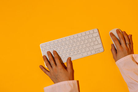 Hands typing on keyboard and mouse over orange backgroundの写真素材