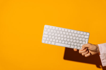 Hand holding wireless keyboard on bright orange backgroundの写真素材