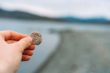 Hand holding small smooth pebble by lakeshoreの写真素材