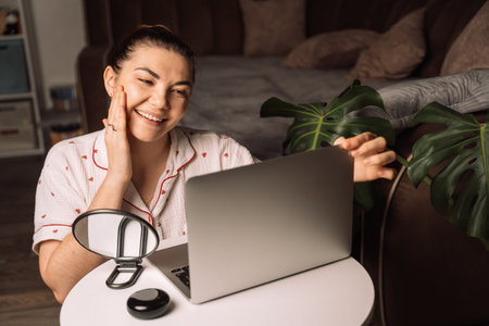 Smiling woman touching face during online call at homeの写真素材
