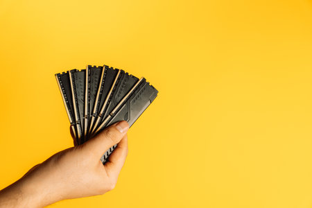 Hand holding fan of black DDR RAM sticks on yellow background, upgrade conceptの写真素材