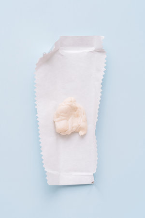 Chewed chewing gum on opened wrapper on blue background, minimal flat lay