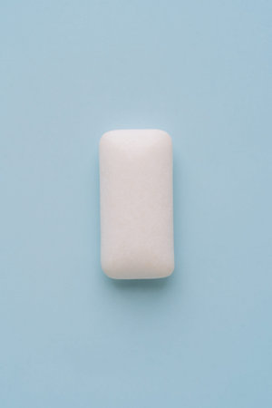 Single white chewing gum piece on light blue background, minimal concept