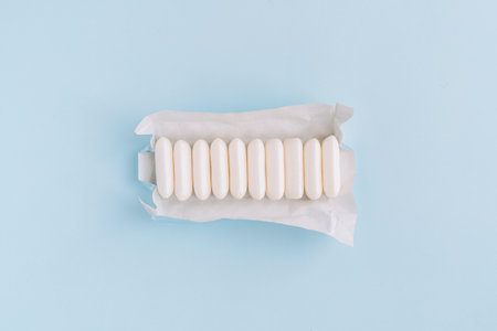 Row of chewing gum pellets in opened wrapper on light blue background