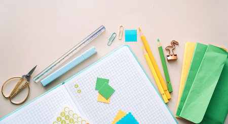 Flat lay of notebook with colorful paper pieces, pens and craft tools, creative planning workspace