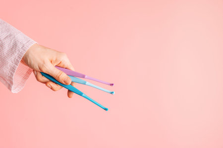 Hand holding three single tuft toothbrushes on pink background, dental hygiene concept with copy...