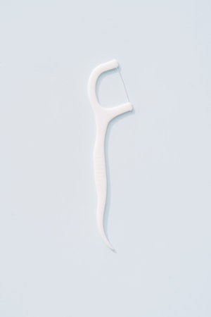 Single white dental floss pick isolated on light blue background, minimal oral hygiene concept