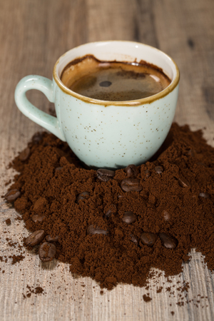 Cup of joy.  Cup of coffee on a handful of grounded coffee mixed with coffee beans on the table indoors.の写真素材