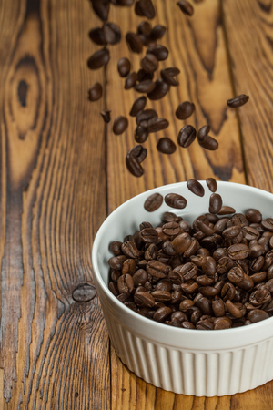 Waiting to be prepared. Shot of roasted coffee beans falling in to a bowl on a texture wooden table.の写真素材