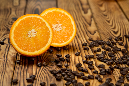 Summer spirit. Shot of a halved orange on a wooden table full of coffee beans spilled around.の写真素材
