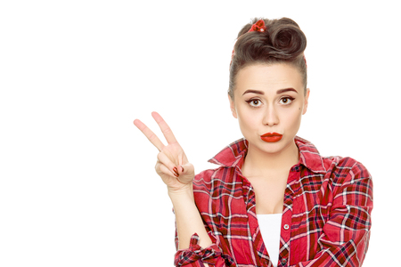 Take two! Young beautiful pinup girl wearing red plaid shirt and vintage makeup showing two fingers or victory sign isolated on white copyspace on the sideの写真素材