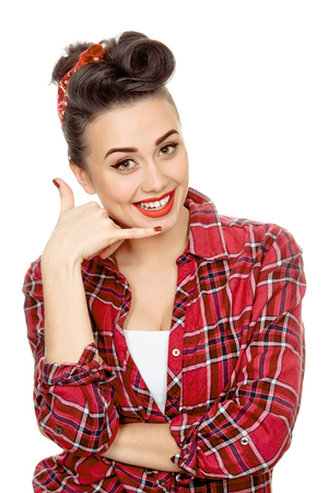 Anytime you need me! Portrait of a beautiful young pinup girl in a plaid shirt wearing a headband and professional retro makeup showing call me gesture isolated on whiteの写真素材