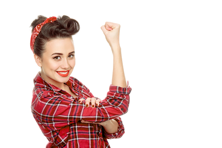 She can do it! Beautiful young pinup woman wearing plaid shirt and a red bandana showing powerful gesture we can do it isolated on whiteの写真素材