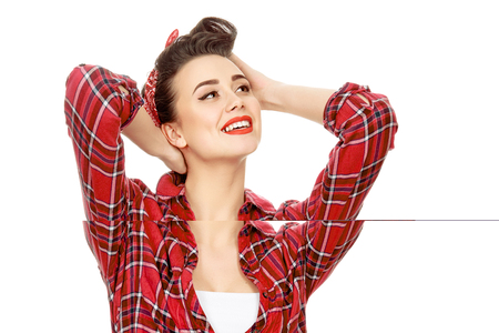 Daydreaming. Shot of a gorgeous brunette with a retro hairstyle and a headband wearing red plaid shirt looking away smiling cheerfully isolatedの写真素材