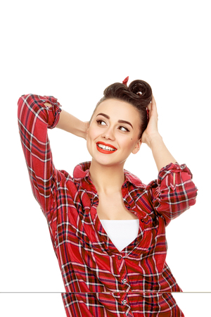 Filled with joy. Vertical portrait of an attractive young pinup girl with vintage hairstyle and makeup smiling looking away joyfully fixing her hair with her hands isolatedの写真素材