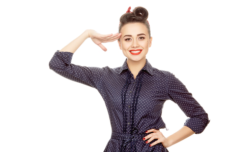 Hey captain! Half length portrait of a gorgeous pinup girl in a dotted dress smiling cheerfully to the camera saluting with her hand isolated on white copyspace on the sideの写真素材