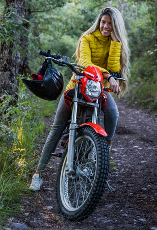young and pretty woman with blonde hair on a motorbike with a yellow jacket and gray jeansの写真素材