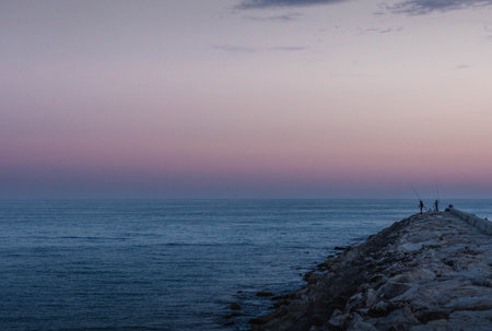 amazing and colorful sunset on the sea in front of a pier with fishermen in the backgroundの写真素材