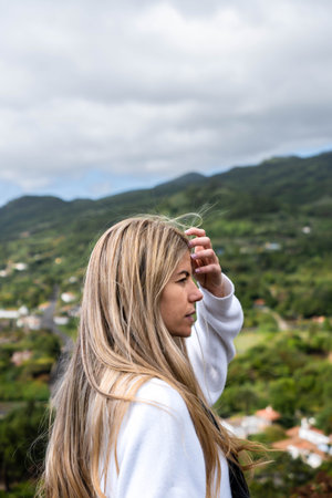 Caucasian woman is touching her long blonde hair in the nature on cloudy dayの写真素材