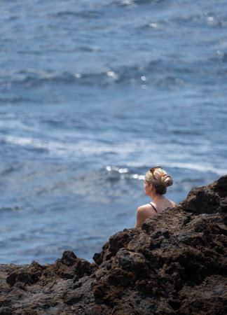 Woman with cue and blonde hair looking the sea. Heavy rocksの写真素材