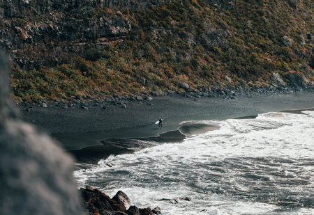 Surfer in the distance. Savage seascape with heavy waves in the beach with black sandの写真素材