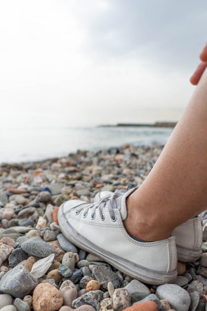 Legs of woman with casual shoes on the pebble or small stones in the beachの写真素材