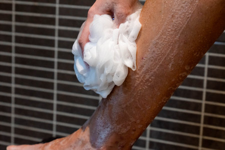 Woman soaping her leg on the shower with white sponge
