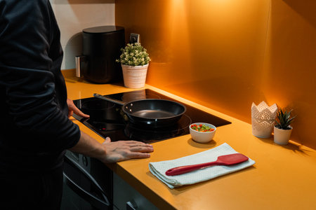 Unrecognizable man switching the induction in orange kitchenの写真素材