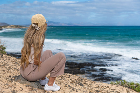 Rear view of sit woman with blonde hair looking at the brave sea, Fuerteventura