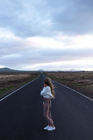 Blonde woman standing in the middle of the road on sunset duskの写真素材