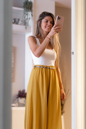 Blonde woman with long hair taking a photo with smartphone in front of mirrorの写真素材