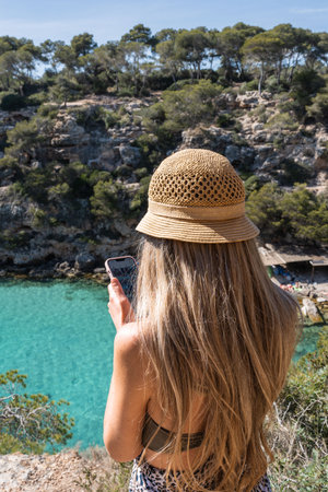 Rear view of blonde woman with smartphone in cala pi, mallorca, balearic islandsの写真素材