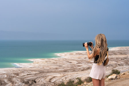 Blonde tourist woman taking a photography of Dead Sea coastline with white salt in Jordanの写真素材