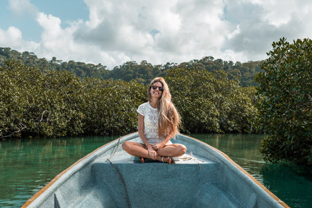 Blonde woman sitting on the edge of a boat floatingの写真素材
