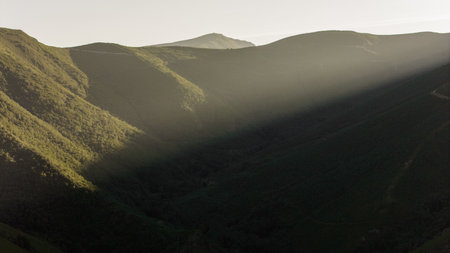 The mountains are covered in trees and the ray of the sun is shining on them