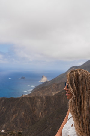 A woman gazes at the coastline from a mountain viewpoint on a cloudy dayの写真素材
