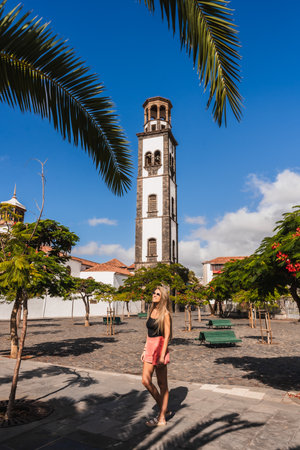 A woman walks through a sunlit square in a historic town with a tall bell towerの写真素材