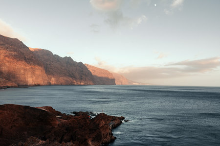 Breathtaking sunset view of rugged cliffs Los Gigantes meeting calm ocean watersの写真素材