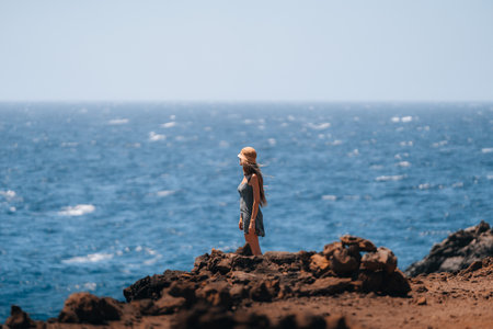 A woman stands on a rocky beach overlooking the oceanの写真素材