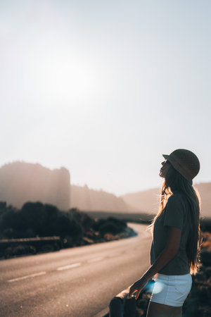 A woman stands by a quiet road, warm sunlight during a serene afternoonの写真素材