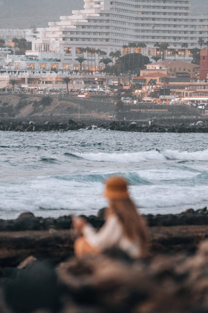 Defocused woman enjoying the coastal view while sitting on rocks near the ocean